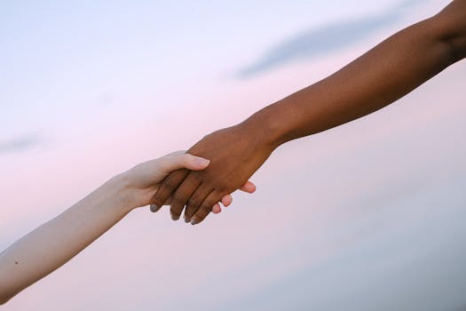 Close-up of diverse hands symbolizing unity and connection against a soft pastel sky.